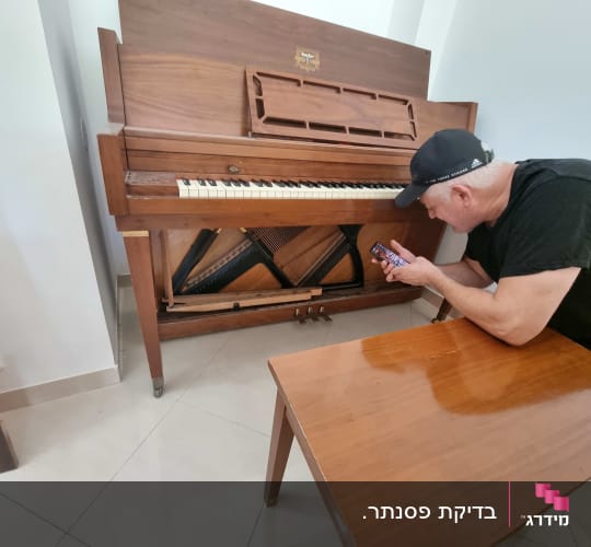 אדם בודק כיוון פסנתר בעזרת טלפון נייד